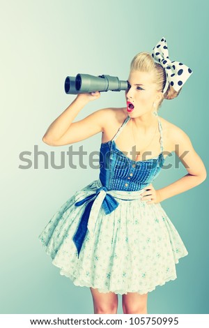 Beautiful young woman with pin-up make-up and hairstyle looking through binoculars.