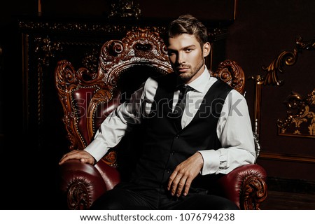 Imposing well dressed man  sitting in an armchair in a luxurious apartments with classic interior. Luxury. Men\'s beauty, fashion.