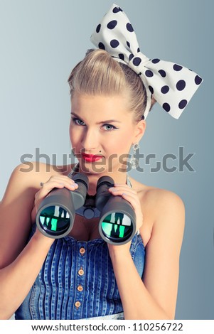 Beautiful young woman with pin-up make-up and hairstyle looking through binoculars.