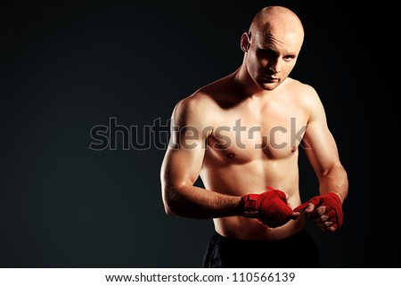 Portrait of a muscular boxer in red gloves posing at studio.
