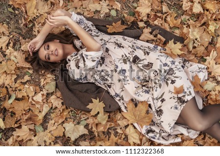 Autumn mood. Beautiful young woman lying on the autumn grass and yellow leaves. Seasonal autumn fashion.