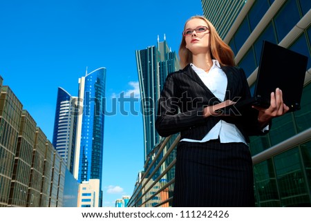Young business woman standing with laptop in the big city and purposefully looking away.