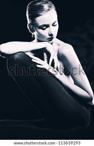 Elegant naked young woman posing over black background. Light and shadow.