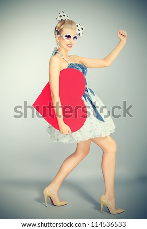 Beautiful young woman with pin-up make-up and hairstyle posing in studio with red heart.