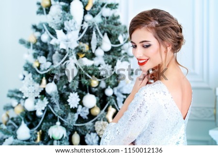 Merry Christmas and Happy New Year. Pretty young woman in evening dress poses near the Christmas tree. Beauty, fashion. Make-up, cosmetics.