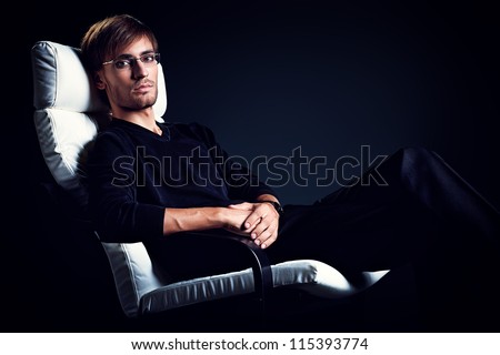 Portrait of a handsome man sitting in the armchair over black background.