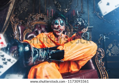 Evil clown man stained in blood is sitting with cigar in a room with vintage interior. Halloween. Horror, thriller film.
