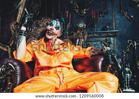 Evil clown man stained in blood is sitting with cigar in a room with vintage interior. Halloween. Horror, thriller film.