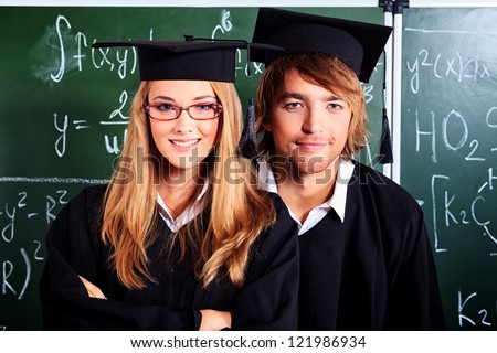 Portrait of a graduating students in an academic gown standing at the classroom.