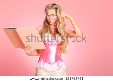 Portrait of a funny blonde woman with a book posing in studio over pink background.