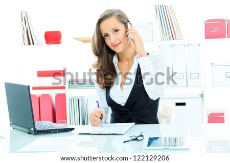Modern business woman is talking on a cell phone at the office.