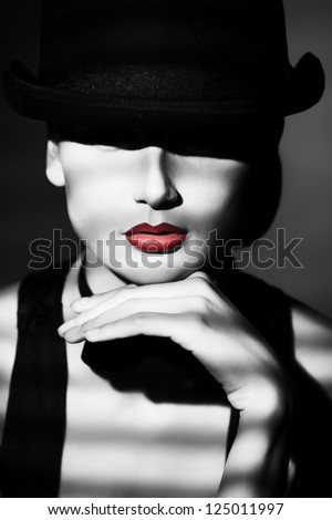 Portrait of the elegant young woman posing in black pot hat. Light and shadow.