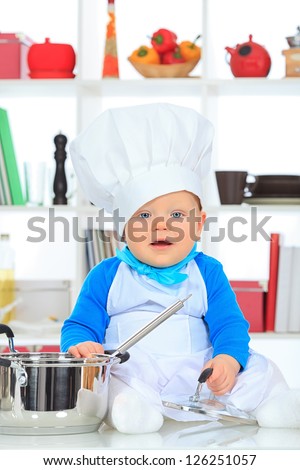 Cute small baby in the cook costume at the kitchen.