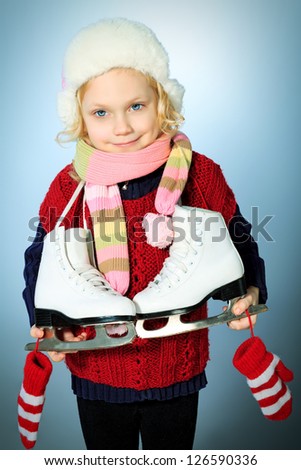 Portrait of a cute little girl in warm hat and sweater posing with figure skates.