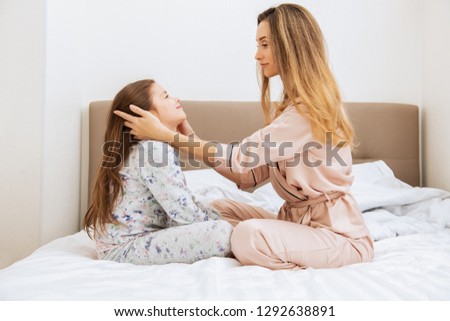 Young woman and her daughter in pajamas are hugging sitting on the bed. Family home shoot.