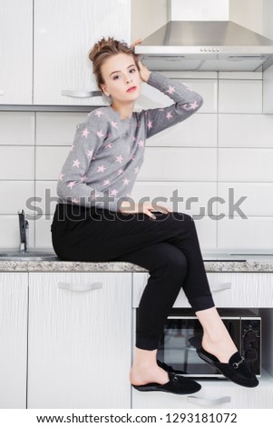 Fashion shot. Beautiful female model is sitting on the countertop of the kitchen set in  home clothes. Beauty, fashion.