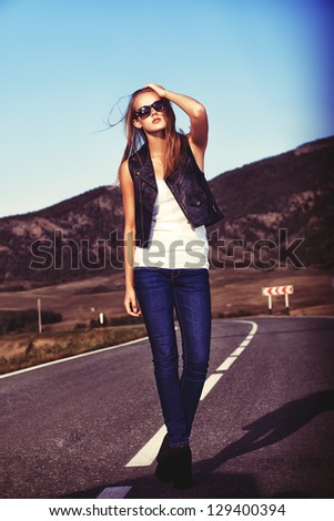 Full length portrait of a beautiful young woman posing on a road over picturesque landscape.
