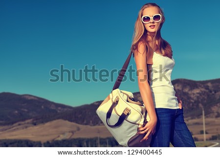 Beautiful young woman posing on a road over picturesque landscape.