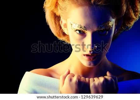 Art fashion photo of a beautiful model with golden make-up. Over black background.