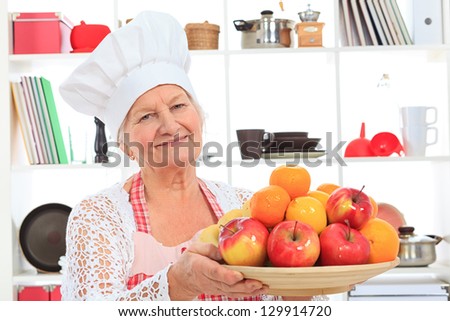 Senior woman chef cook standing with a plate of fruits in the kitchen.