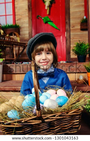Happy little boy with bunny is standing on the porch near the wooden house. Easter holiday. Rural style, easter decoration.