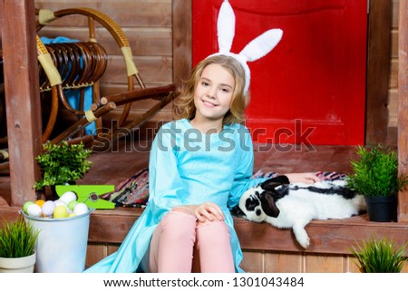 A happy little girl is sitting on the porch near the wooden house. Easter holiday. Rural style, easter decoration.