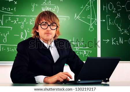 Portrait of a smart male student in a suit working on a laptop at a classroom.