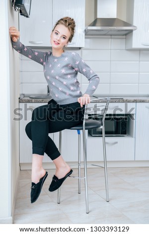 Fashion shot. Beautiful female model is sitting on a bar stool of the kitchen set in  home clothes. Beauty, fashion.