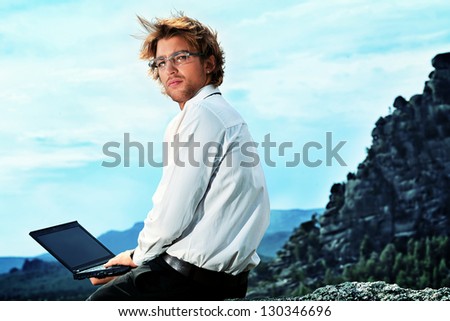 Successful business man working on a laptop on a peak of the mountain.