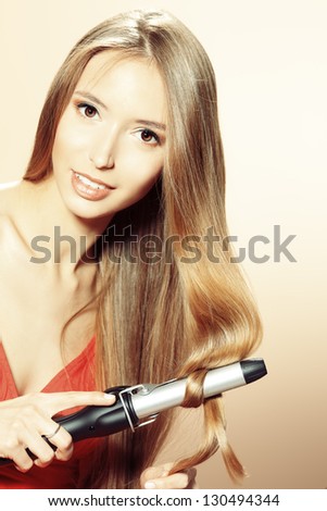 Beautiful young woman doing hairstyle with curling irons.