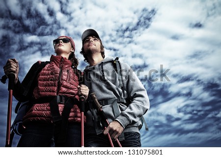 Couple of tourists are standing at the top of a mountain and looking into the distance.