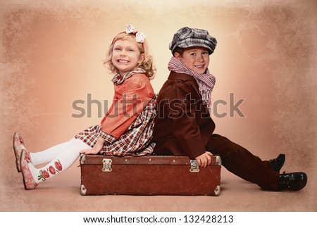 Cute little boy is sitting on the old suitcase with charming little lady. Retro style.