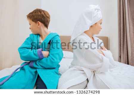 Cute girl and boy lie in bathrobes in bed at home. Fashion home shot. Childhood. Kid\'s fashion.