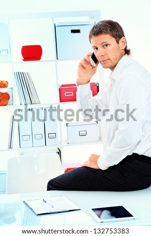 Handsome businessman is talking on a cell phone at the modern office.