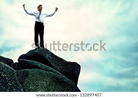 Successful business man standing on a peak of the mountain and purposefully looking away.