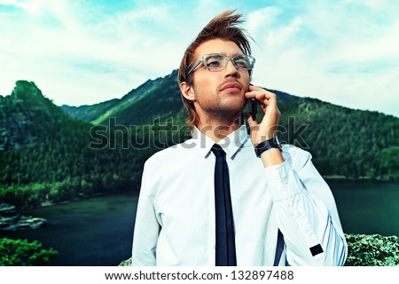 Successful business man standing on a peak of the mountain and talking on the phone.