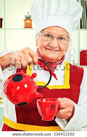 Portrait of a senior woman chef cook making tea in the kitchen.
