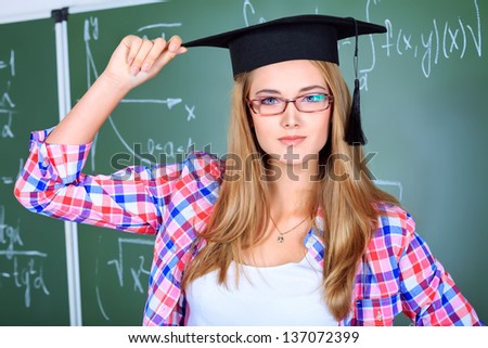 Portrait of a graduating student girl in an academic hat standing at the classroom.