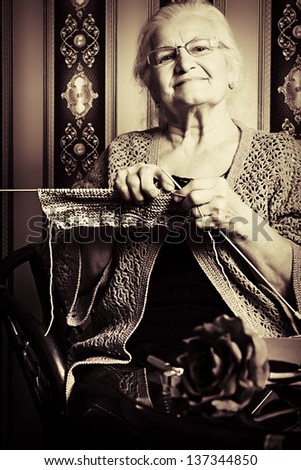 Portrait of a smiling senior woman knitting on spokes at home. Old-fashioned style.