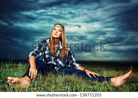 Romantic young woman in casual clothes sitting in a field on a background of the storm sky.