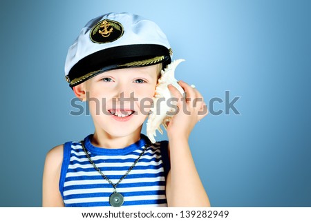 Little smiling sailor boy is listening to the sound of the sea in the shell.
