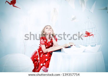 Beautiful little girl dreaming with her book and red paper bird in a birdcage.