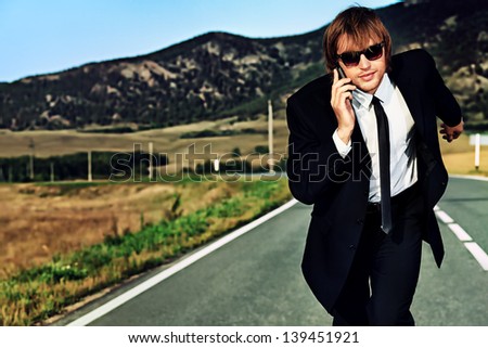 Businessman is running on the highway and talking on a mobile phone. Business struggle concept.