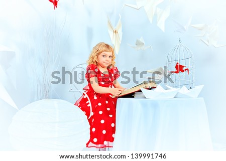 Beautiful little girl dreaming with her book and red paper bird in a birdcage.
