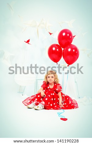 Cute little girl sitting with red balloons in a white room surrounded with paper birds.
