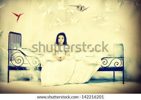 Pretty little girl sitting on her bed surrounded by paper birds. Dream world.