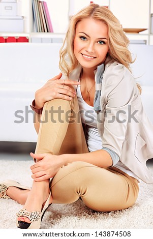 Portrait of a pretty blonde woman sitting on the floor at home.