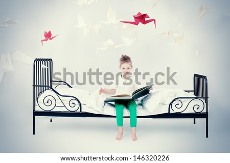 Cute little boy sitting on the bed and reading fairy tales. Dream world.