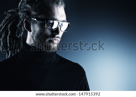 Portrait of a modern handsome young man in spectacles over dark background.