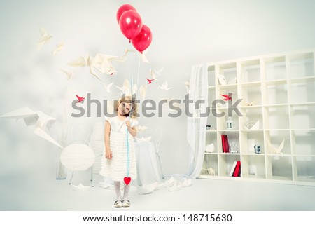 Cute little girl standing with red balloons in a white room surrounded with paper birds.